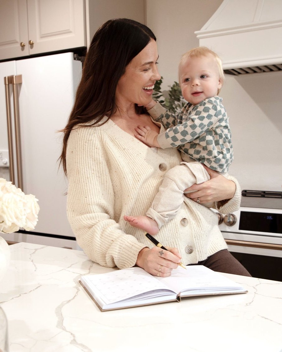 woman with her baby in the kitchen writing in her agenda